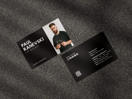 Two-sided black barber business card mockup showing photo and name front with social icons QR code and shop contact reverse