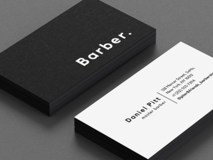 Close-up of minimal black and white personal barber business card template showing bold BARBER text on the front face
