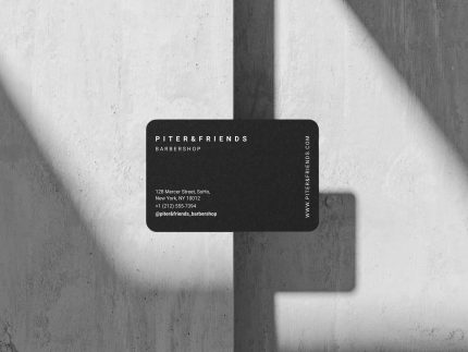 Two versions of a minimalist barbershop business card template — black and white — displayed side by side on a dark flat-lay surface