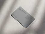 Minimal grey barbershop card placed on a raw concrete or stone surface inside a loft-style industrial barbershop interior